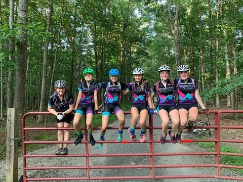 Girl mountain bikers sitting on a red fence, looking fly and happy. 