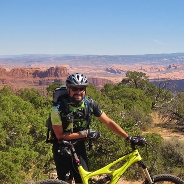 a mountain biker leaning against a bike, with a western canyon landscape in background