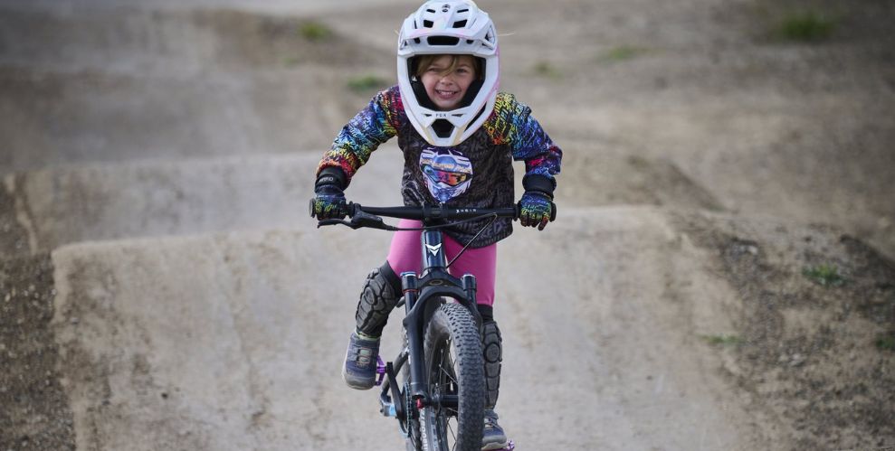 little girl mountain biker in full face mask riding with huge grin on pump track. 