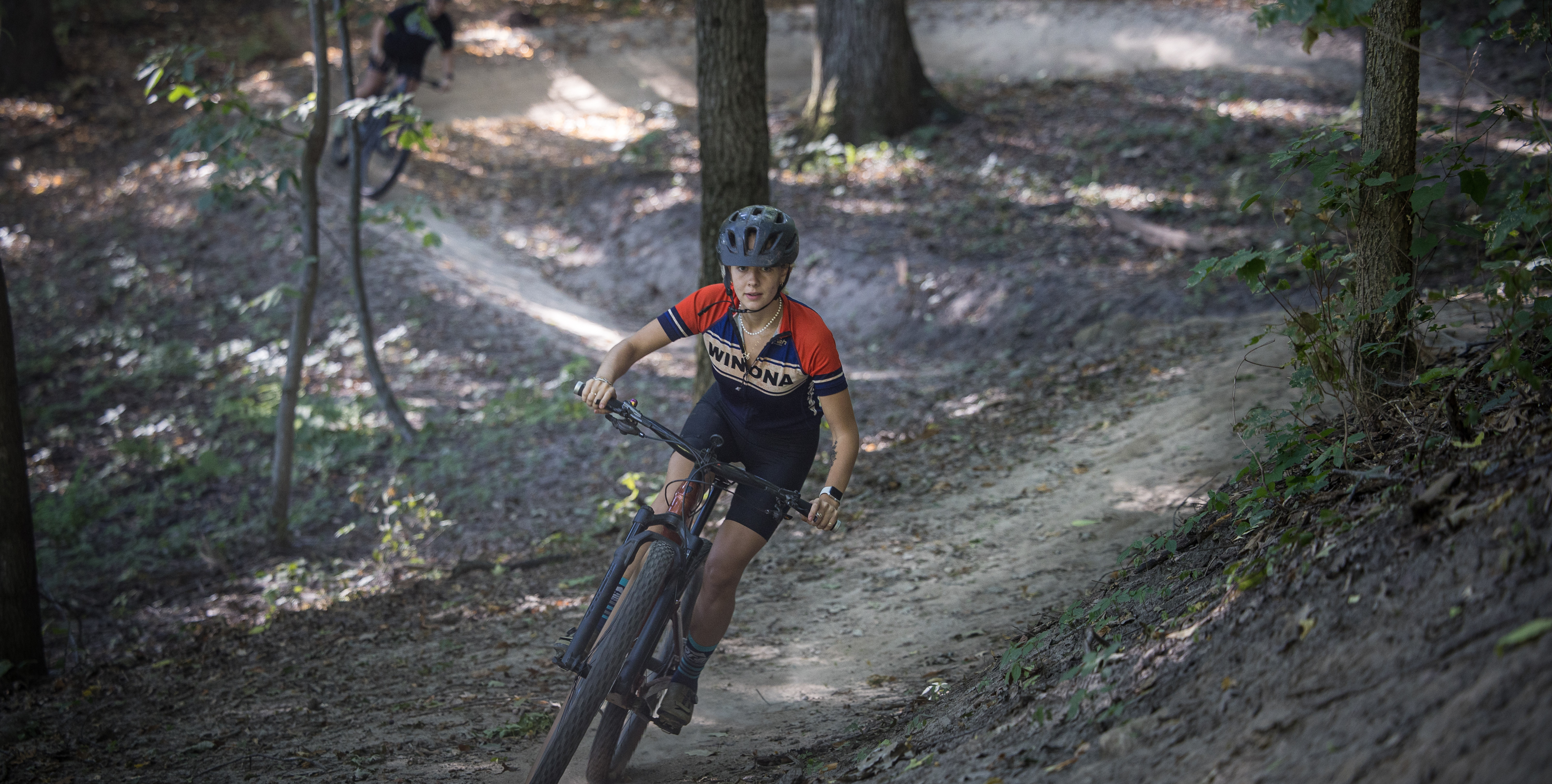 MTB rider wearing a Winona jersey riding on a wooded trail