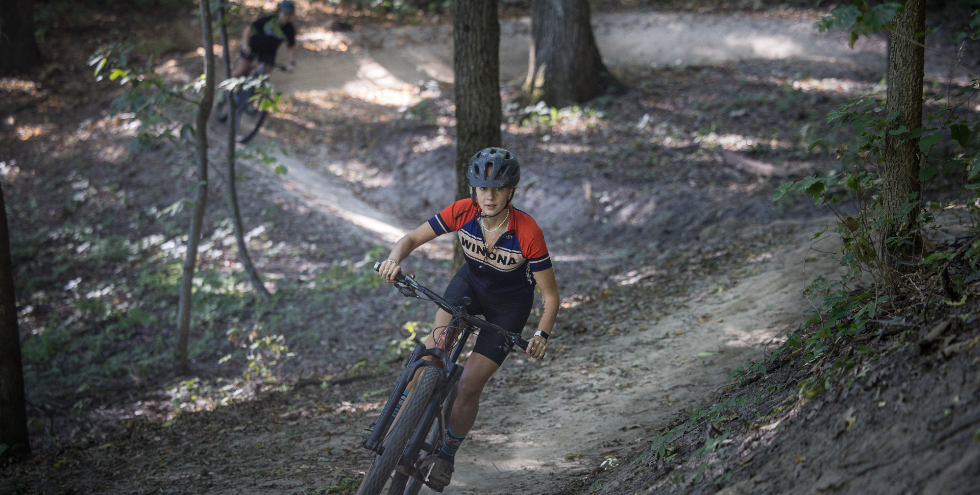 MTB rider wearing a Winona jersey riding on a wooded trail