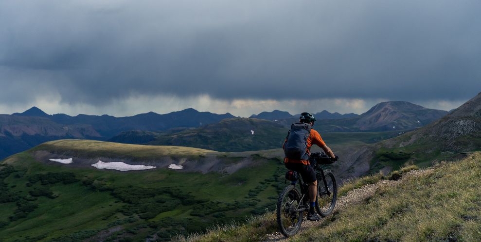 mountain bikers riding away from camera, into cloudy skies on long distance trails