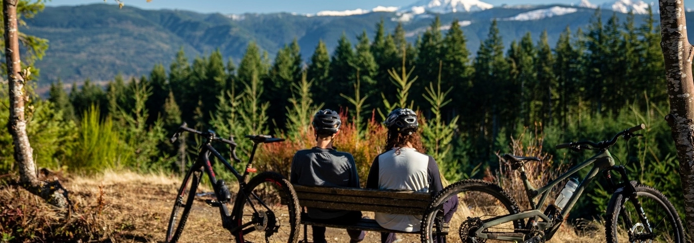 Two bikers sit on a bench on a trail system in West Virginia, looking out at the view. 