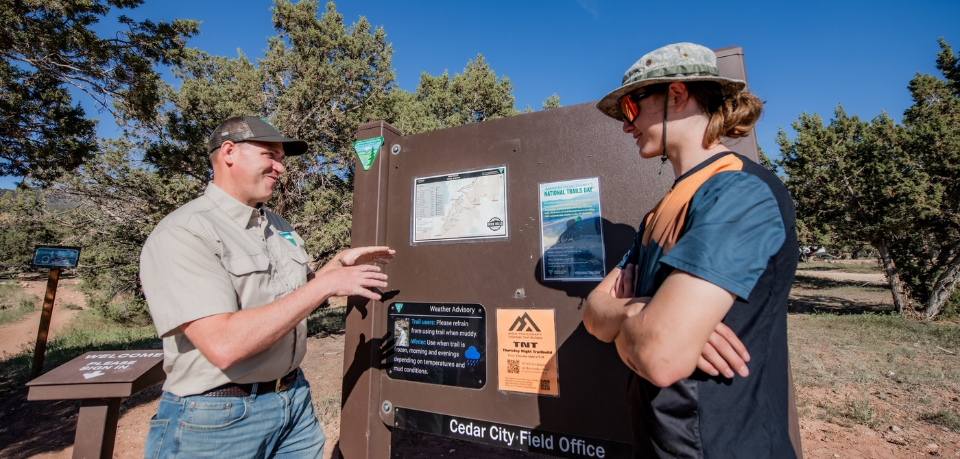 land manager and trail user talk near a trail kiosk