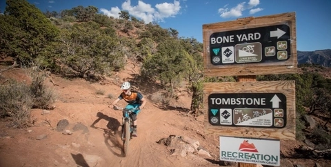 Mountain biker riding by clear signage for trails in Cedar City, Utah.