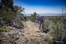 Two female trail builders perform hand work in a desert environment.
