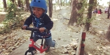  Little guy wearing blue helmet having the time of his life on a red Strider 12” Sport.